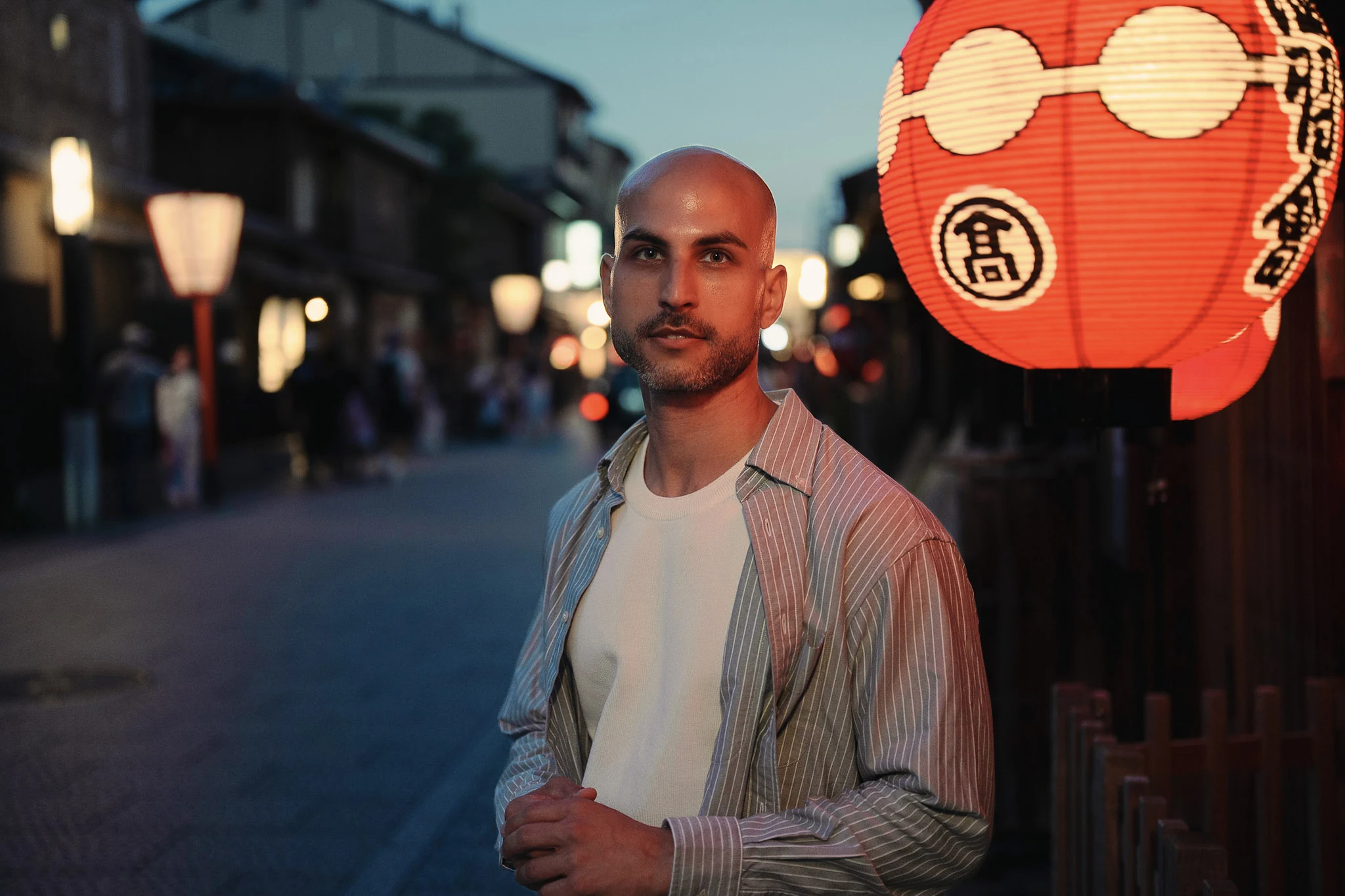 Man standing beside a glowing red lantern on a Japanese street at dusk