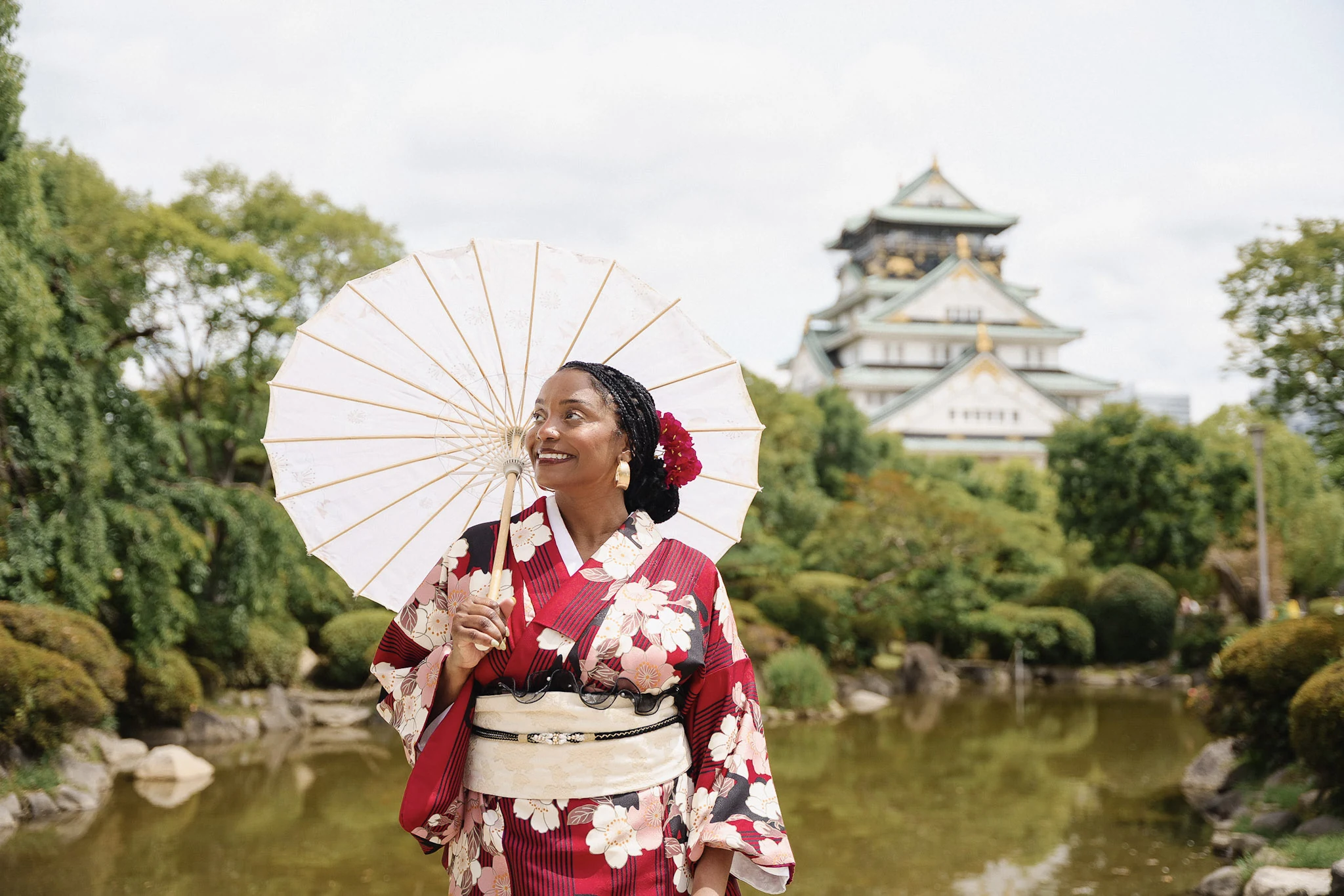 Woman in a red floral kimono holding a white parasol beside Osaka Castle